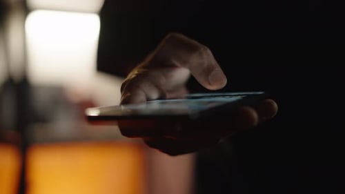 Man's Hand Scrolls on Smartphone in Dark Environment