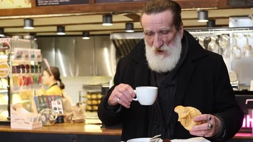 Senior Man Enjoys Coffee and Croissant at Cafe