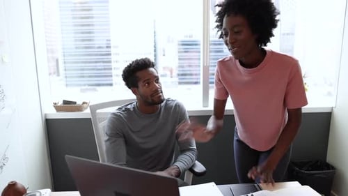 Two Young Adults Discussing Work at Desk in Office