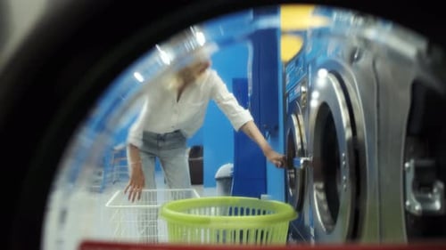 view through the washing machine door, a woman takes out washed clothes