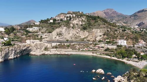 Scenic coastal town with rocky hills and clear blue waters, shot from above