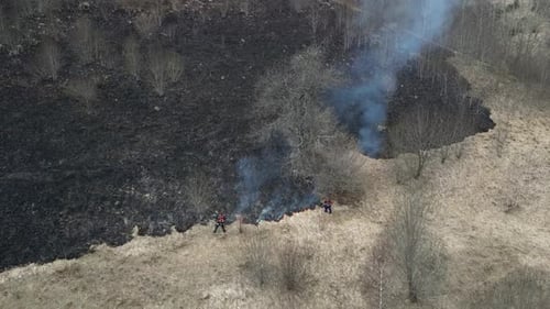Two firemen extinguish a fire. Burning field. Wildfire in the mountains. Forest fire.