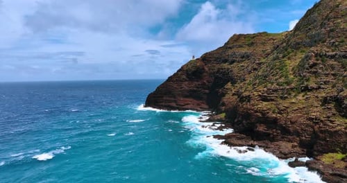 Flight above the azure waterscape along the bare cliffs. Little lighthouse is on the rock.