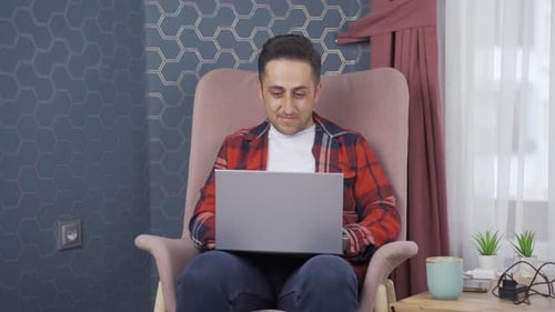 Man Working on Laptop in Chair at Home