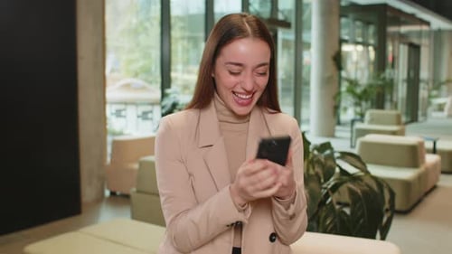 Happy Amazed Businesswoman Using Smartphone Shocked By Sudden Victory Lottery Win in Office Lobby