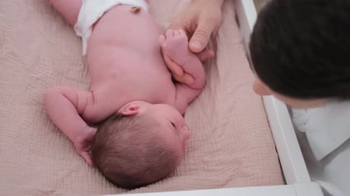 A Parent Carefully Swaddles Her Baby on a Soft Mat in a Bright Nursery