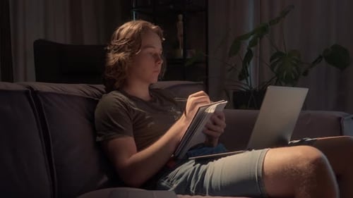 Student lernt spät in der Nacht und macht sich Notizen von einem Laptop in einem dunklen Raum