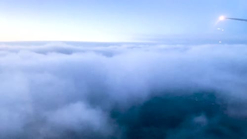 Plane descending through thick blue clouds at blue hour. View of sea of clouds from airplane window.