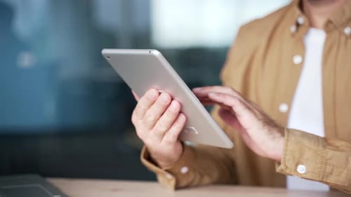 Close up of male hands holding digital tablet at desk at workplace in modern business office.