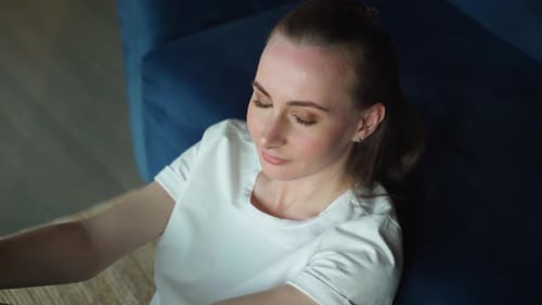Young Woman is Sitting on the Floor in the Living Room Thinking About the Question with a Thoughtful