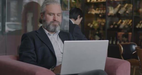 Mature Businessman in Suit Working with Laptop Computer Sitting in Armchair in Cafe