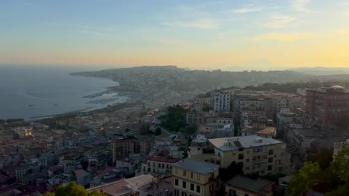 A sweeping view of a coastal city during dawn or dusk, with buildings densely packed on a hillside o