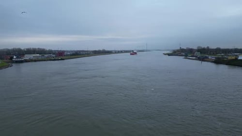 Flying Above River Towards Container Ship On A Cloudy Day In Dordrecht, Netherlands. wide aerial