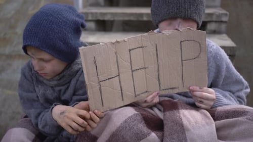 Homeless Boys Sit with a Help Sign on the Stairs in an Abandoned Place A Homeless Children with a