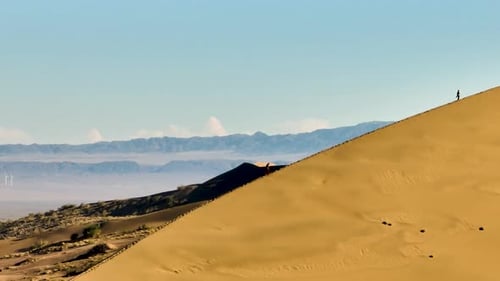 Two people climbing a massive desert sand dune under a blue sky