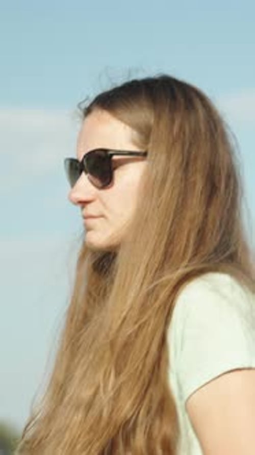 A woman walks through a sunlit field during the day, holding a bouquet of Lagurus. Vertical