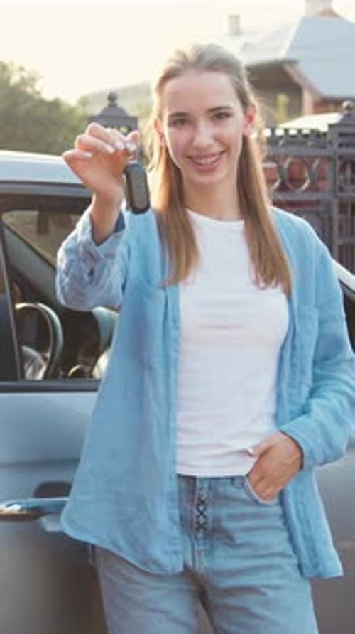 Happy Adult Woman Showing Keys Standing on Her New Electric Car Outdoors on the Street While