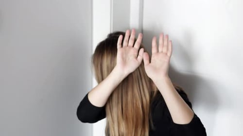 Young Adult Covers Face with Hands Near Wall