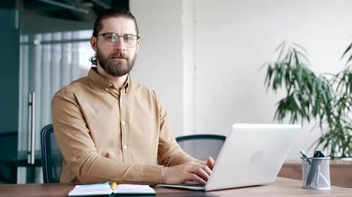 Porträt eines lächelnden IT-Spezialisten, der am Schreibtisch am Arbeitsplatz in einem modernen Geschäftsbüro sitzt