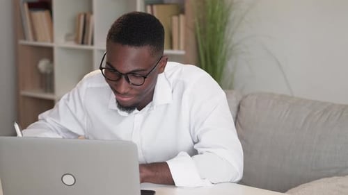Man Working at Home Using Laptop and Writing