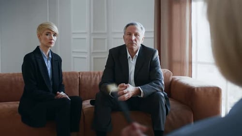Un couple est assis sur un canapé lors d'une conversation avec une autre personne filmée dans un cadre intérieur