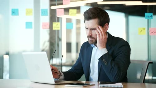Overworked businessman suffering from headache working on a laptop at workplace in business office.