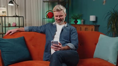 Mature Man Using Phone on a Living Room Couch