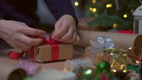 Closeup View Female Hands Tie Red Bow Ribbon on Wrapped Christmas Gift Box
