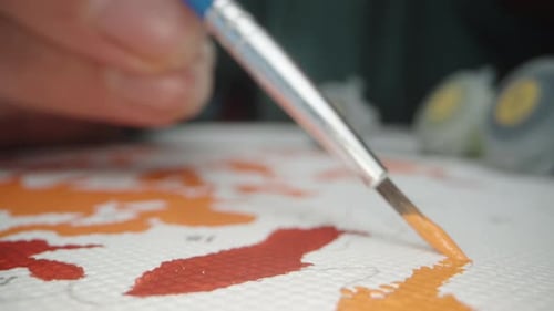 Close-up, a girl paints a picture with numbered areas with a brush and paints.