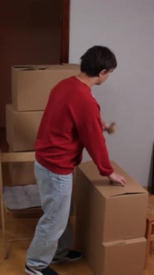 Vertical Video Closeup Man Packing Cardboard Boxes in New Apartment During Moving Day