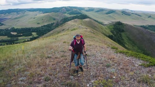 Middleaged Male Tourist with a Large Backpack Walks Along a Hilly Ridge