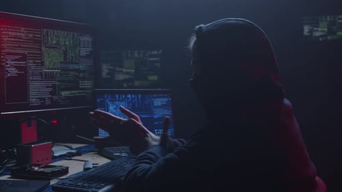 Hooded Person Typing on Computer in Dark Room