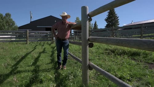 Homme mûr au chapeau de cowboy s'appuyant sur une clôture dans un ranch