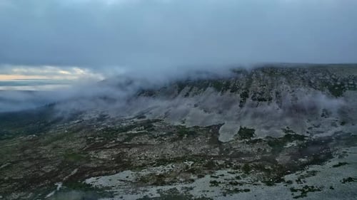 Aerial side view steep slope of mountain ridge covered with clouds evening sky