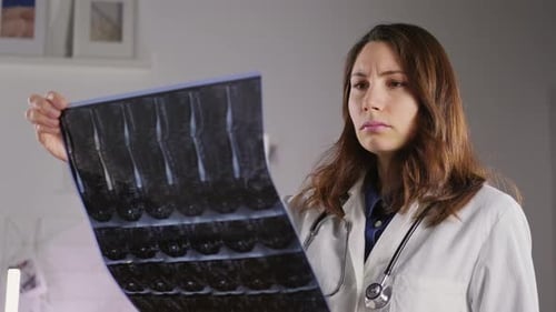 A Young Female Doctor Holds an Xray of the Bones of the Spine and Examines It