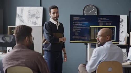 Multiethnische männliche Entwickler analysieren Code auf dem Bildschirm während einer Bürobesprechung