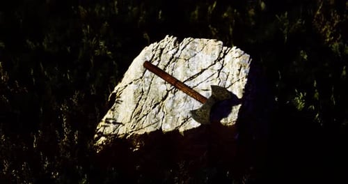 Hacha rústica que descansa sobre una piedra desgastada en un entorno cubierto de hierba al anochecer
