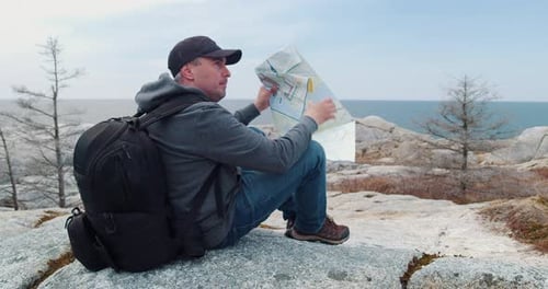 Man Reads Map on Rocky Ocean Coastline