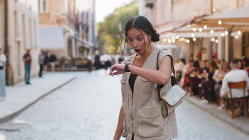 Shocked Woman Checks Watch on Cobblestone City Street
