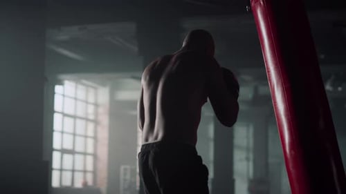 Athletic man training with heavy bag in dark gym