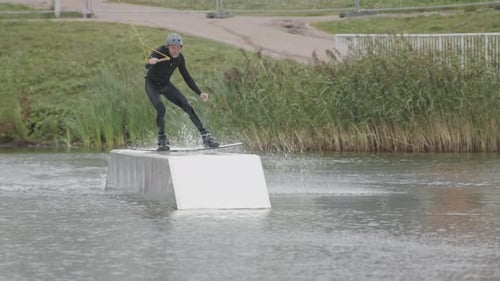 Man Wakeboarding and Jumping Over Platform on Lake