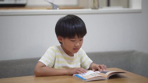 Boy Reading Book Indoors at Wooden Table
