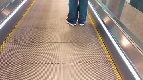 View of person's feet and legs standing on moving walking escalator at Bangalore airport, close up s