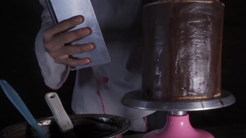 Confectioner Smoothing Chocolate Frosting on Cake