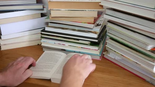 Ein nicht wiederzuerkennender Mann liest ein Buch mit Stapeln von Büchern auf dem Schreibtisch. Er blättert um und liest
