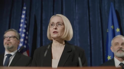 Blonde Woman Gives Speech at Podium with Flags