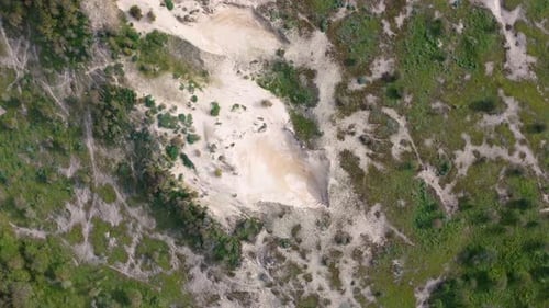 Aerial view of a sandy area surrounded by green vegetation and trees, showcasing a natural landscape