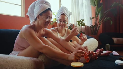 Women painting toenails and relaxing on sofa