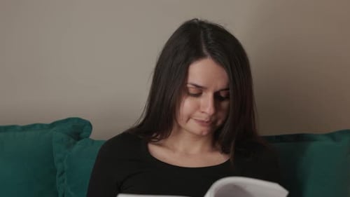 Eine Frau, die auf dem Sofa sitzt und in den Seiten eines Buches versunken ist - Nahaufnahme