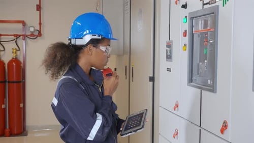 Woman Inspecting Electrical Panel with Walkie Talkie and Tablet